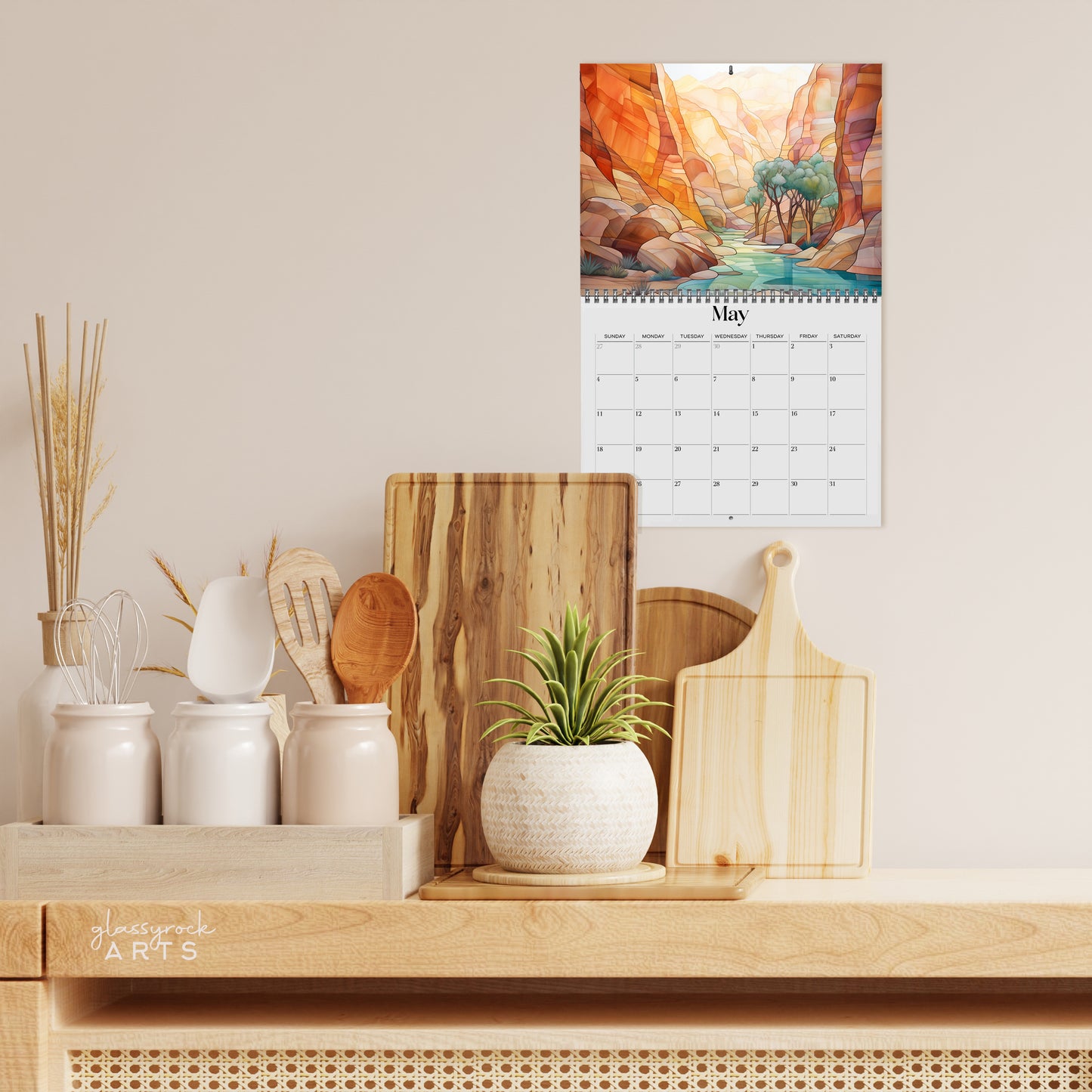 The 2025 Wall Calendar - Stained Glass Desert Landscapes, with spiral binding and a centered hole for hanging, features vivid desert illustrations. 