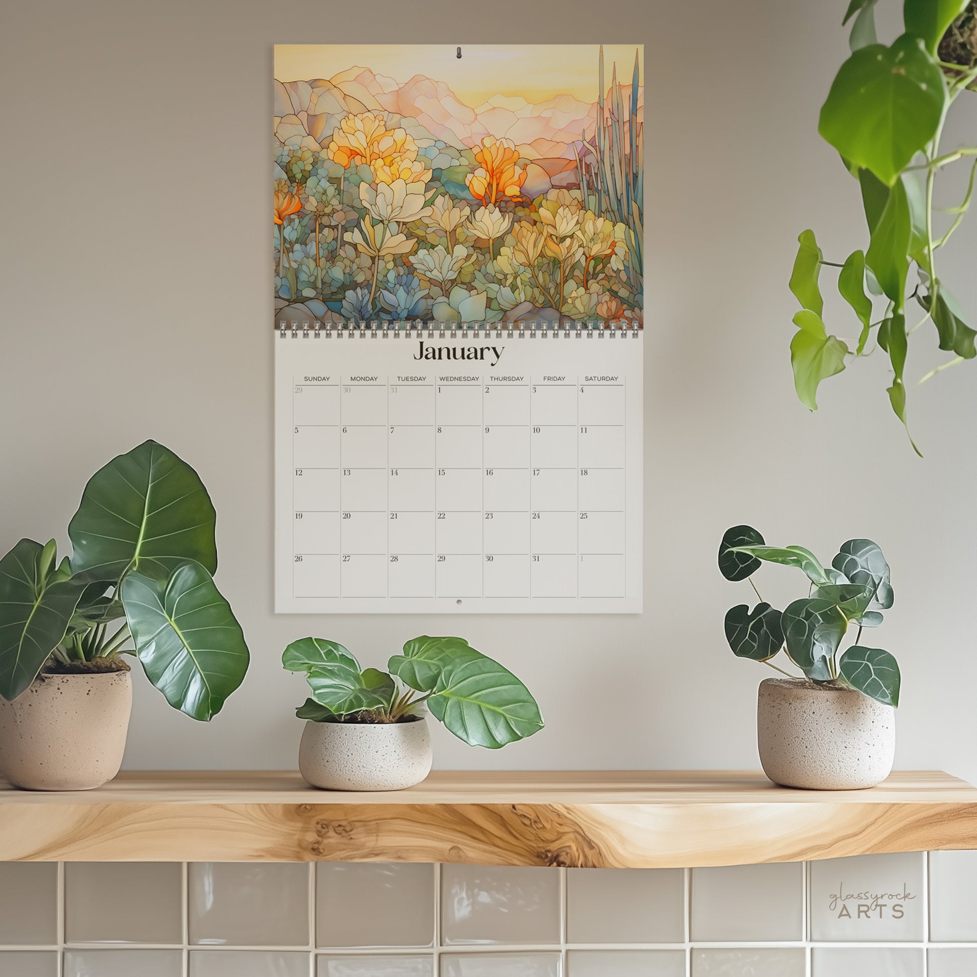 The 2025 Wall Calendar - Stained Glass Desert Landscapes, with spiral binding and a centered hole for hanging, features vivid desert illustrations. 