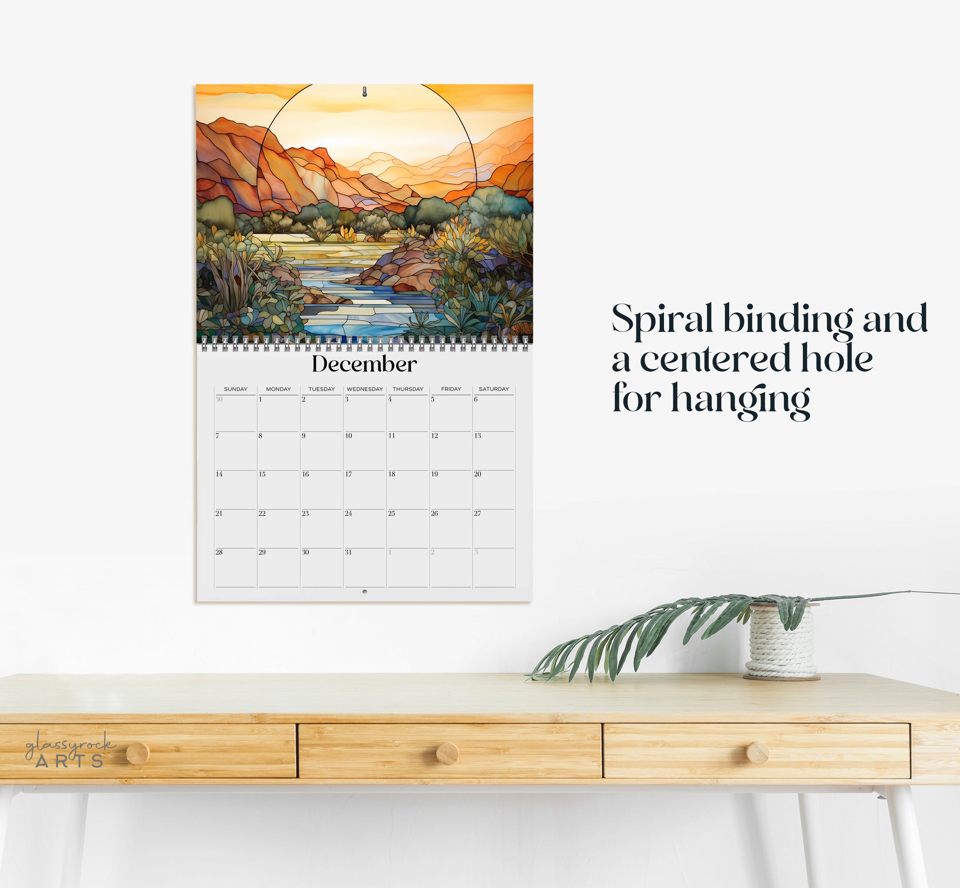 The 2025 Wall Calendar - Stained Glass Desert Landscapes, with spiral binding and a centered hole for hanging, features vivid desert illustrations. 