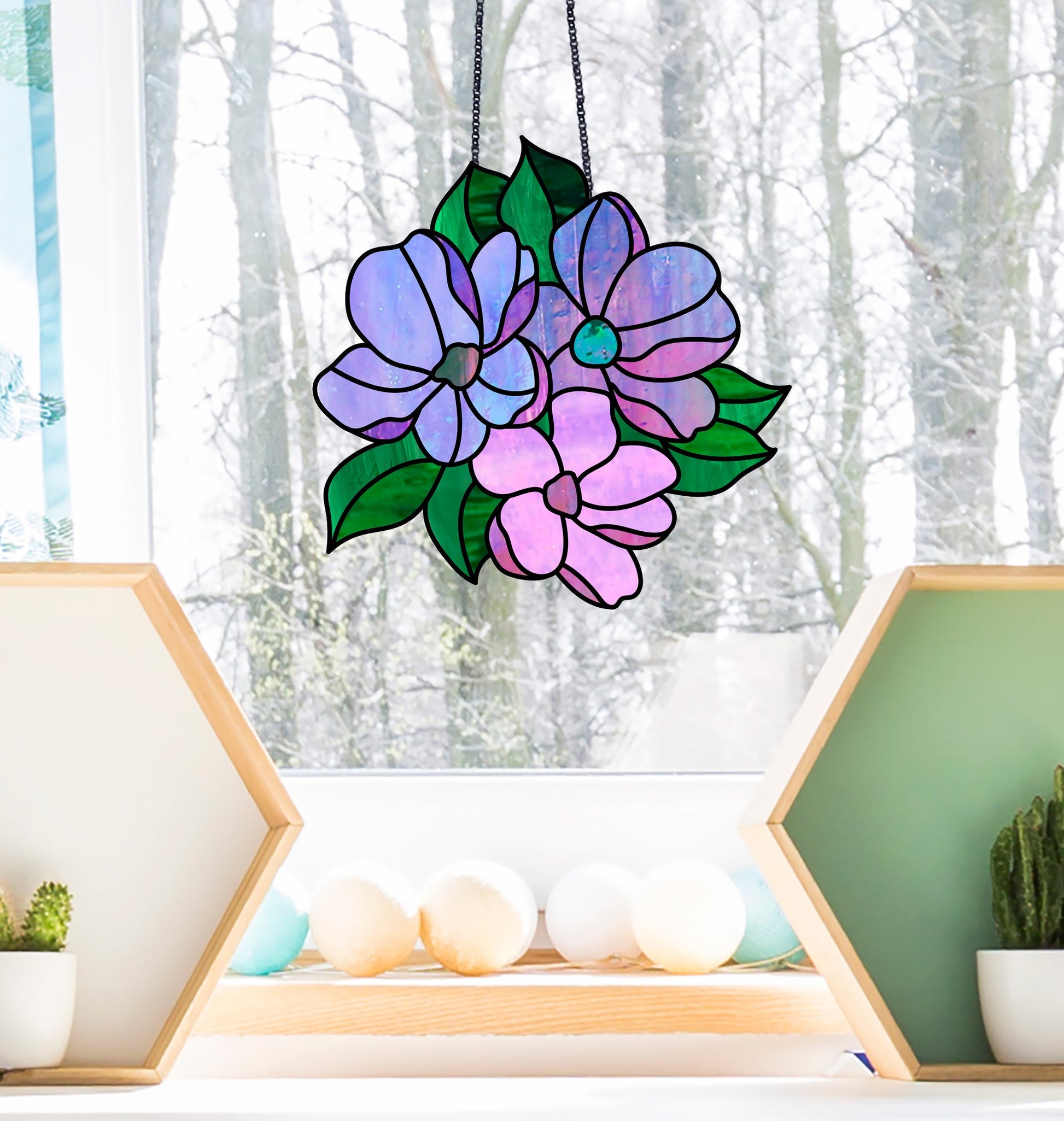 The Bundle of Flowers Stained Glass Pattern, showcasing purple and pink flowers with green leaves, decorates a window. Outside, snow blankets the ground, while small geometric shelves with plants and decor enhance the scene indoors.