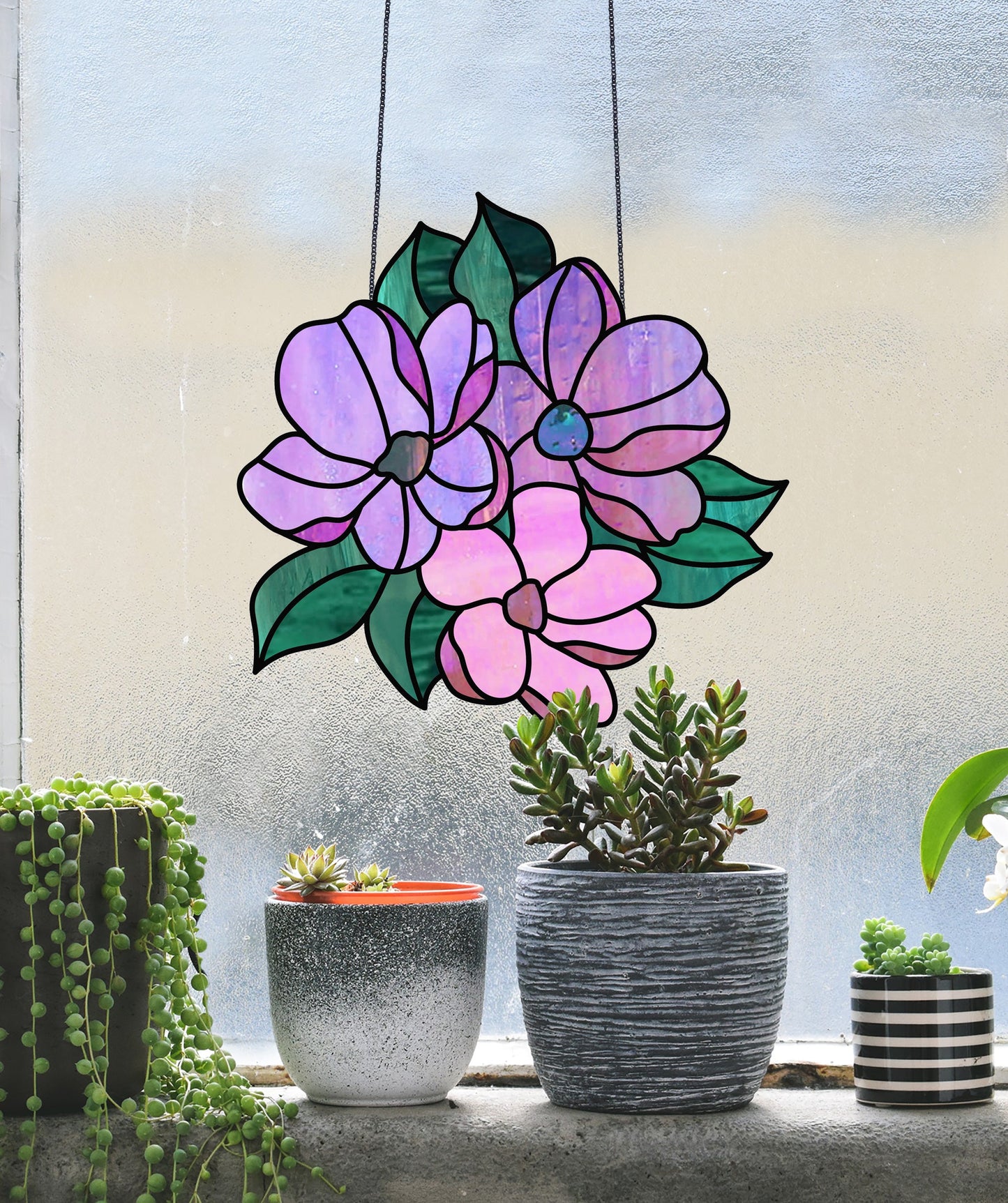 A Bundle of Flowers Stained Glass Pattern suncatcher with purple and pink blooms decorates the frosted window, while three potted plants, including succulents and trailing greenery, are charmingly arranged on the sill.