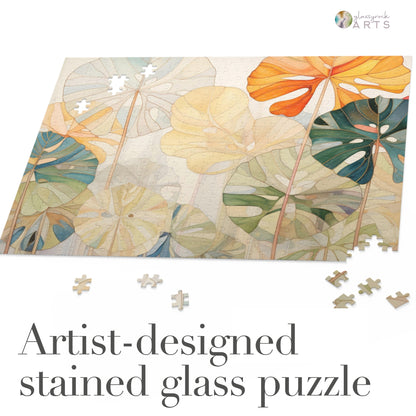 The Stained Glass Monstera Leaves Jigsaw Puzzle showcases a vibrant floral design with orange, green, and beige leaves. Loose pieces are scattered nearby. Text reads, “Artist-designed stained glass puzzle.” An ideal unique art gift for couples to enjoy together.