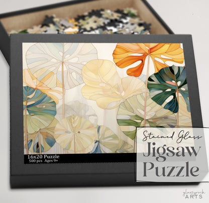 The Stained Glass Monstera Leaves Jigsaw Puzzle, featuring a vibrant green, orange, and beige leaf design, measures 16x20 inches with 500 pieces. Its the perfect art gift for couples or anyone aged 9 and up.