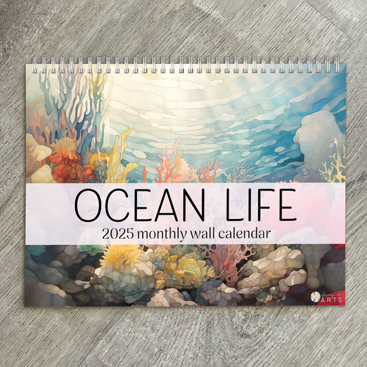 The ocean life calendar, a 2025 monthly wall calendar with ocean-themed original artwork, on a wood table surface. 