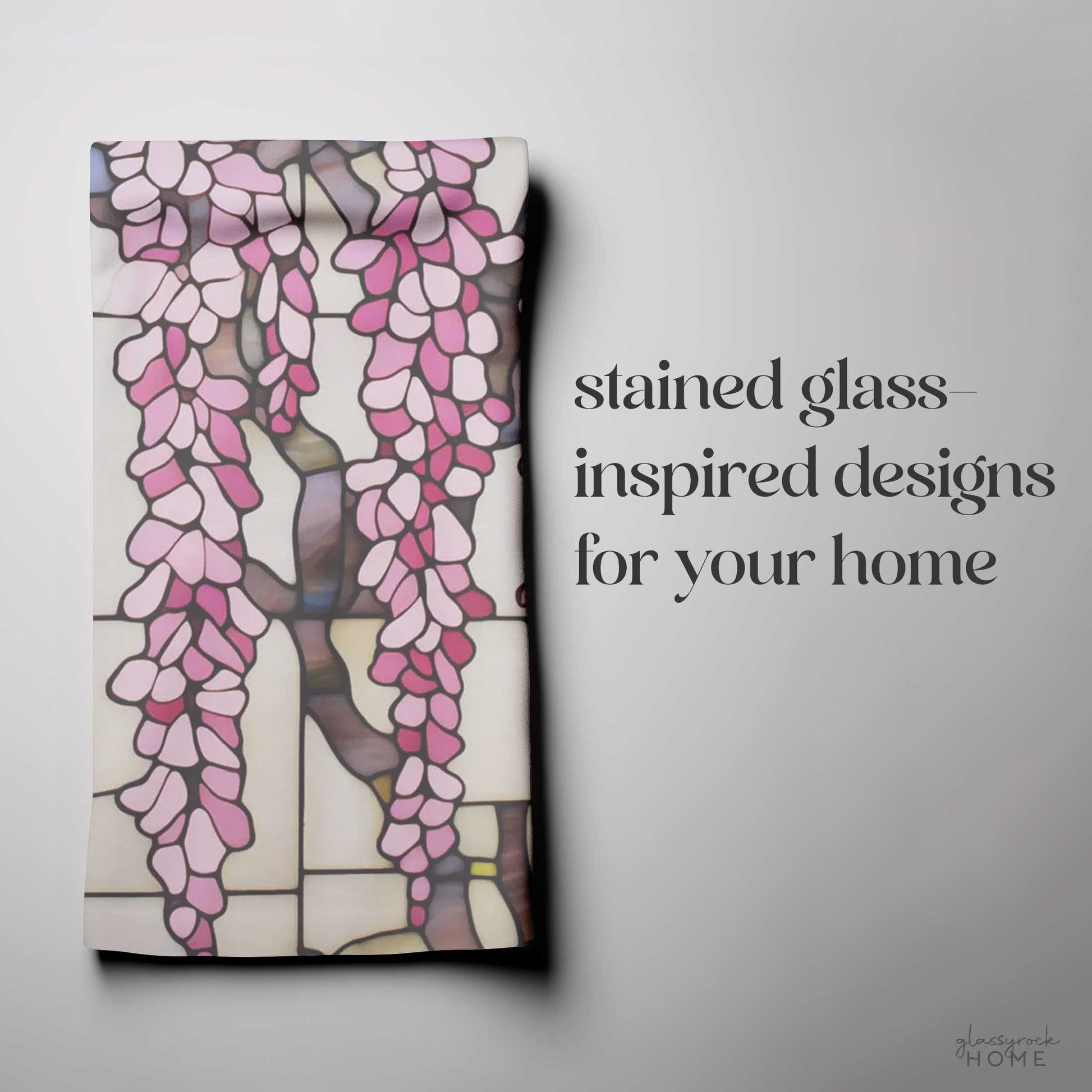 The Stained Glass Pink Wisteria Dish Towel, showcasing a folded fabric with pink stained glass-inspired patterns and an original pink wisteria design, is displayed next to the text "stained glass-inspired designs for your home" on a white background.