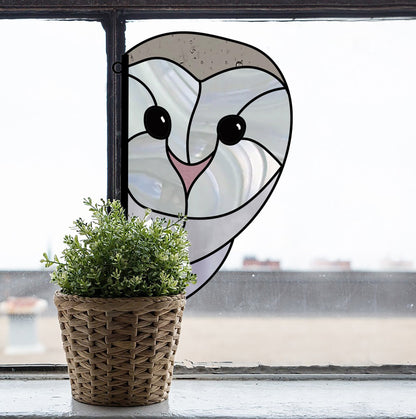 A Snowy Owl Stained Glass Pattern in neutral tones adorns the window, paired with a small woven basket containing a green plant on the sill. The blurred scene beyond enhances the charm and mystery of this delightful view.