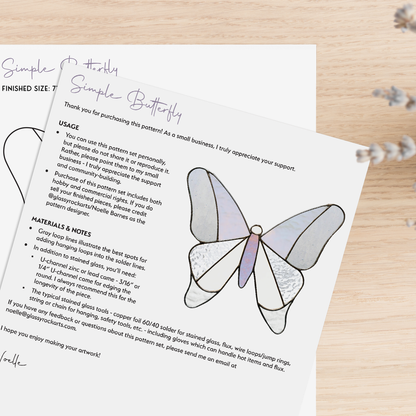 Two pages of the simple butterfly stained glass pattern on a wood table with lavender.