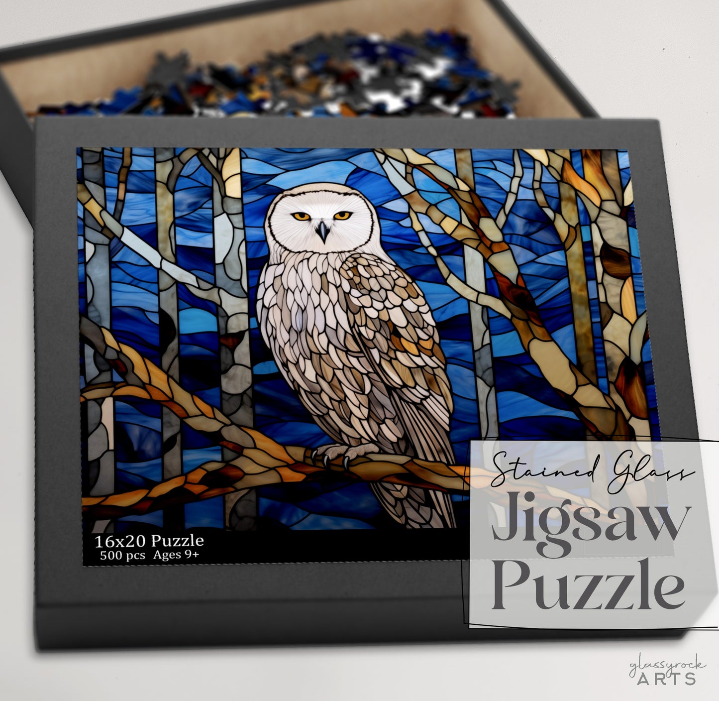 The Stained Glass Owl Jigsaw Puzzle is a 500-piece set ideal for puzzle lovers aged 9 and up, featuring an owl perched on a branch with blue and orange abstract trees in the background.