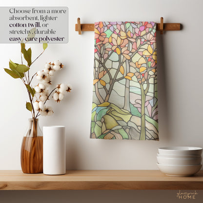 The Stained Glass Spring Forest Dish Towel with a vibrant tree pattern hangs on a wooden rack, paired with a cotton plant, white paper towels, and stacked bowls. Text reads: Opt for absorbent cotton twill or stretchy, durable polyester.