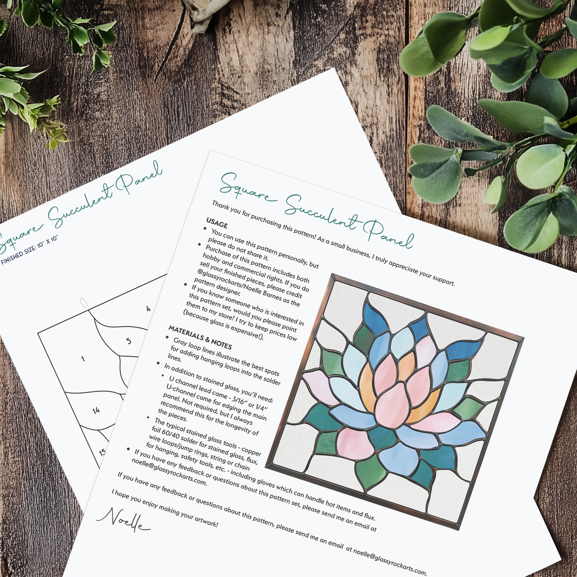 Two pages of the square succulent panel stained glass pattern, laying on a wood table with plants.