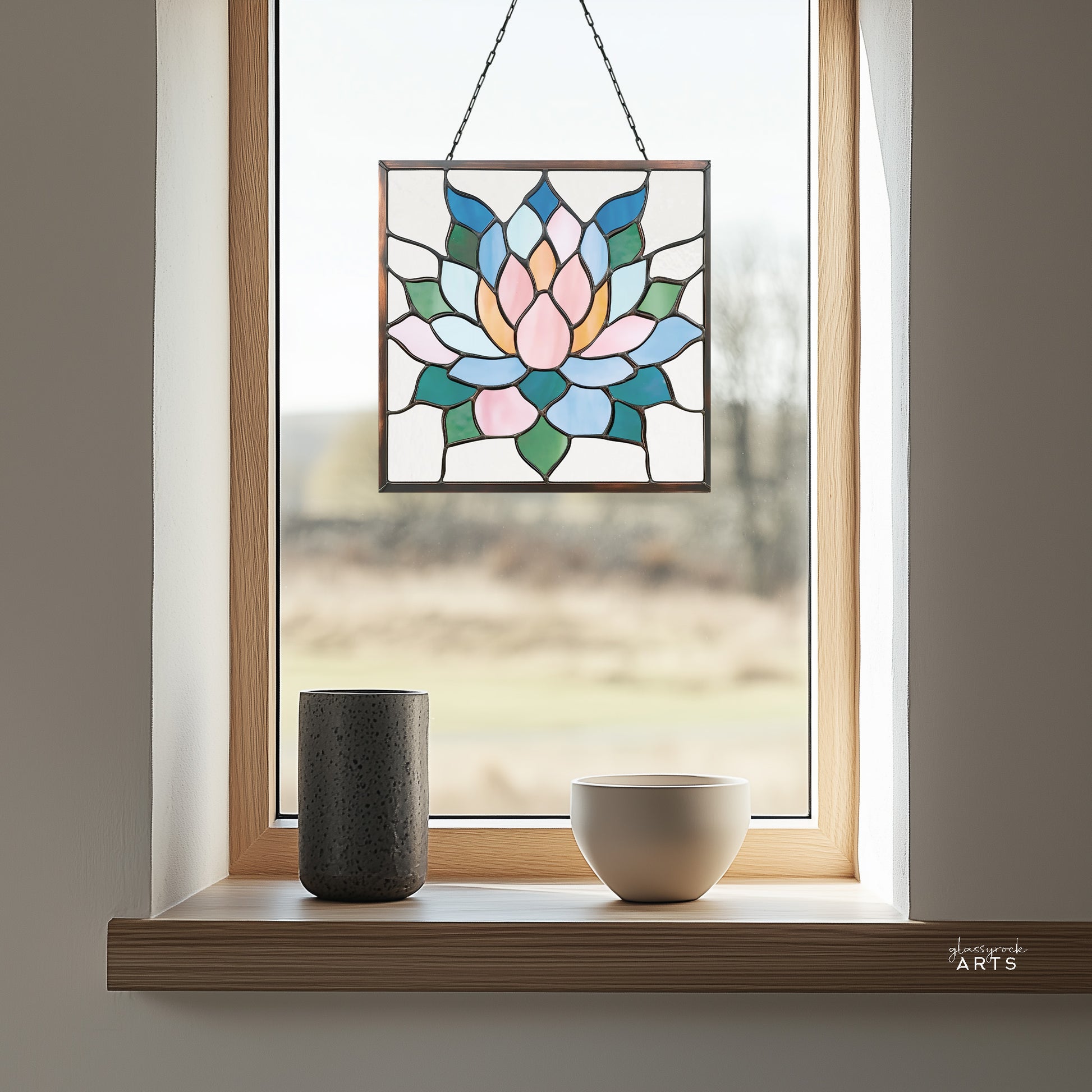 A beautiful square stained glass succulent panel, hanging in a window with a green trees background and two vases on the windowsill.