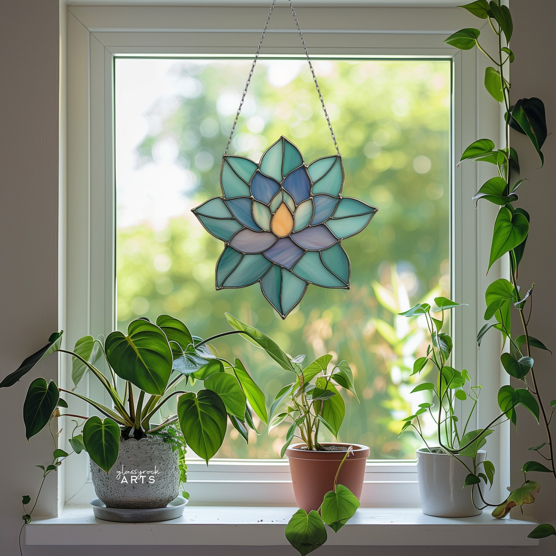 A colorful succulent suncatcher hanging in front of a window that has trees outside. The windowsill is full of plants. 