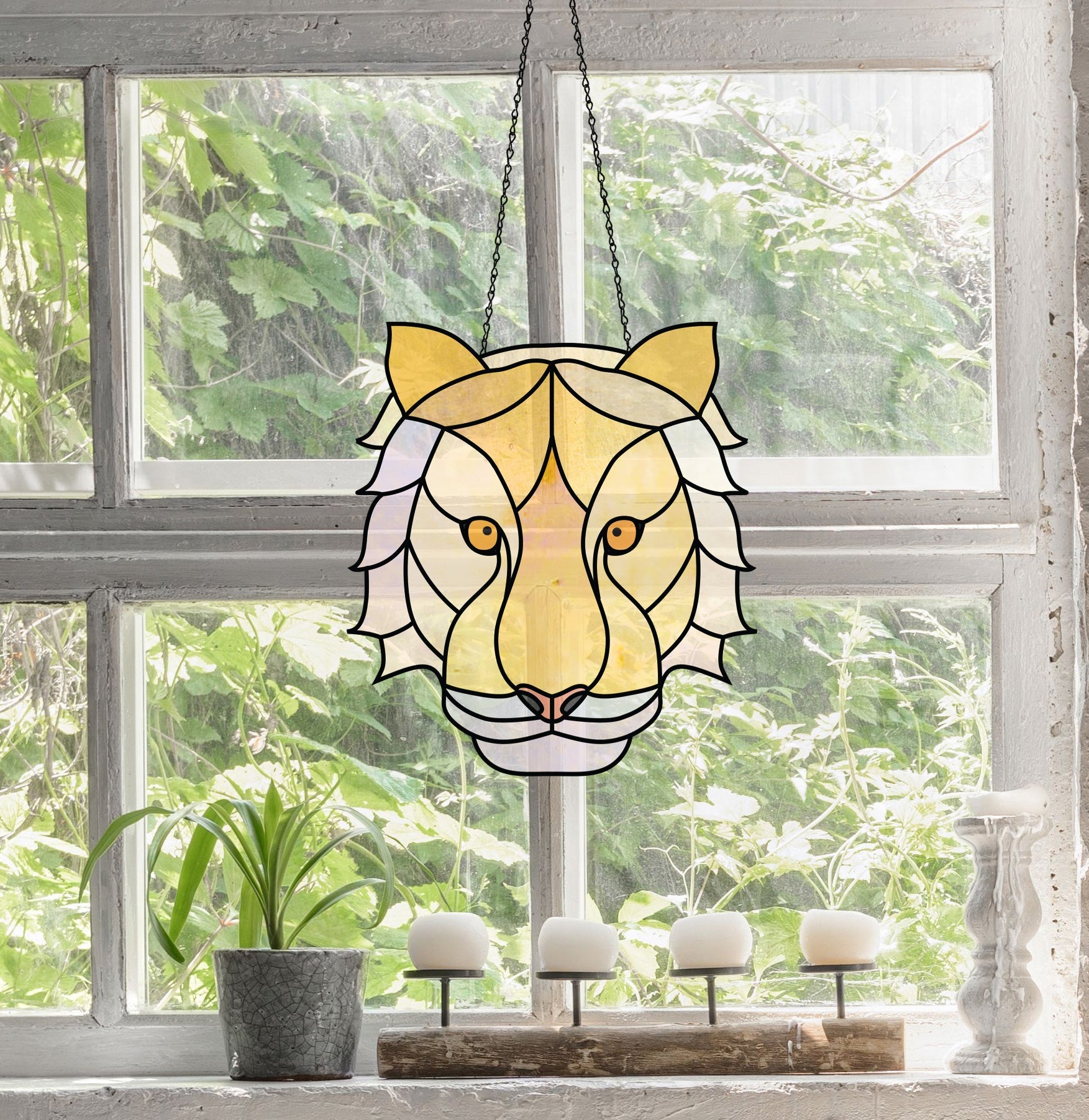 The Tiger Eyes stained glass pattern, exuding boho charm, hangs in front of a sunlit window. Below it, four white candles sit on a stand next to a small green plant with lush foliage visible outside.