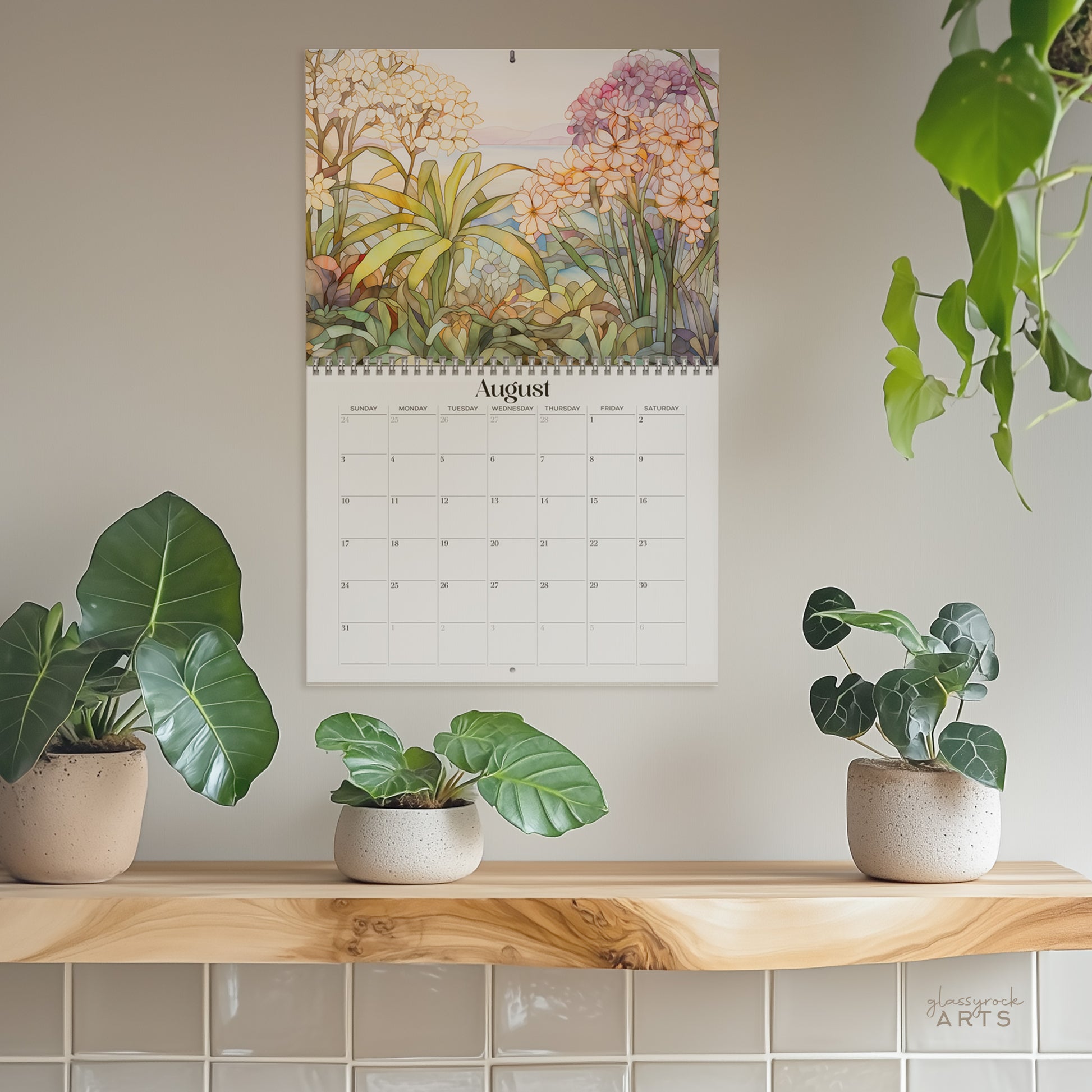 A wall calendar displaying the month of August hangs above a wooden shelf holding potted plants. The 2025 Wall Calendar - Stained Glass Tropical Blooms, crafted from high-quality paper, features beautiful tropical flower illustrations at the top.