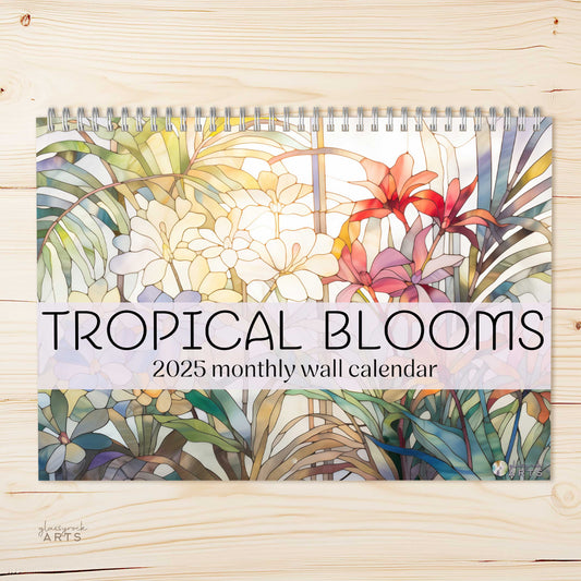 A 2025 wall calendar titled "Stained Glass Tropical Blooms" displayed on a wooden surface, featuring a colorful design of tropical flower illustrations on the cover and printed on high-quality paper.