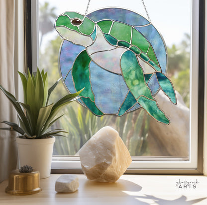 The Round Stained Glass Turtle Pattern sun catcher adorns a sunny window, surrounded by succulents and crystals, with sunlight streaming through to cast colorful patterns and enhance the decor.