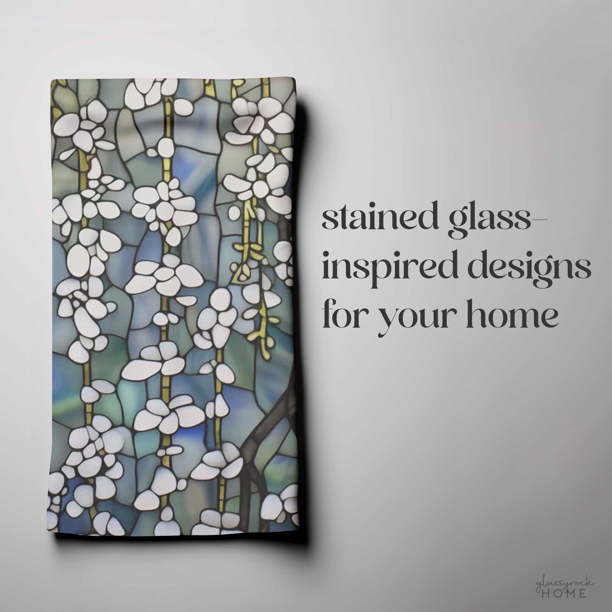 Folded cloth with white and green stained-glass-inspired floral patterns. Text reads: "stained glass-inspired designs for your home." Available in easy-care polyester, the Stained Glass White Wisteria Dish Towel adds a touch of elegance to any room.