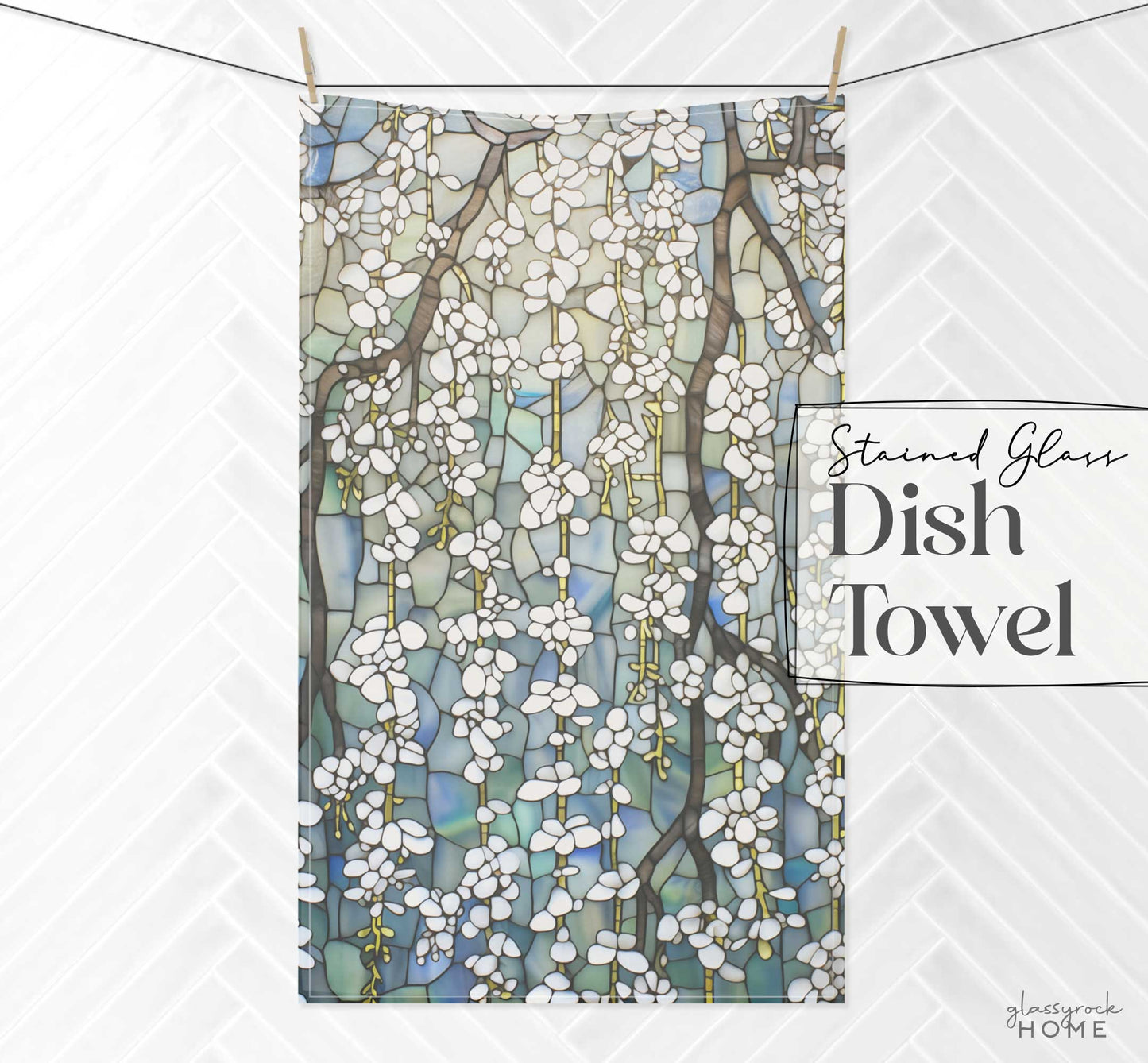 A dish towel hanging on a line features a design resembling stained glass with white flowers and branches on a blue and green background. Made from easy-care polyester, the text reads "Stained Glass White Wisteria Dish Towel.