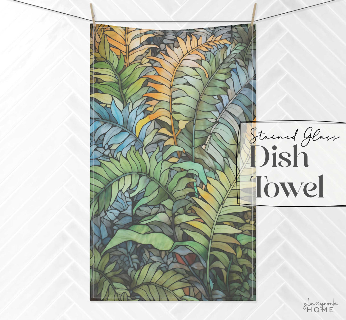 A stained glass kitchen towel featuring a vibrant, tropical leaf design in shades of green, blue, and yellow hangs against a white tiled background. Made from easy-care soft polyester, this towel is labeled "Stained Glass Wild Ferns Dish Towel.