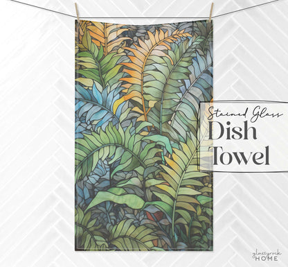 Dish towel featuring a stained glass-style design of overlapping blue, green, and yellow tropical leaves on a white herringbone-patterned background. The text reads Stained Glass Wild Ferns Dish Towel.