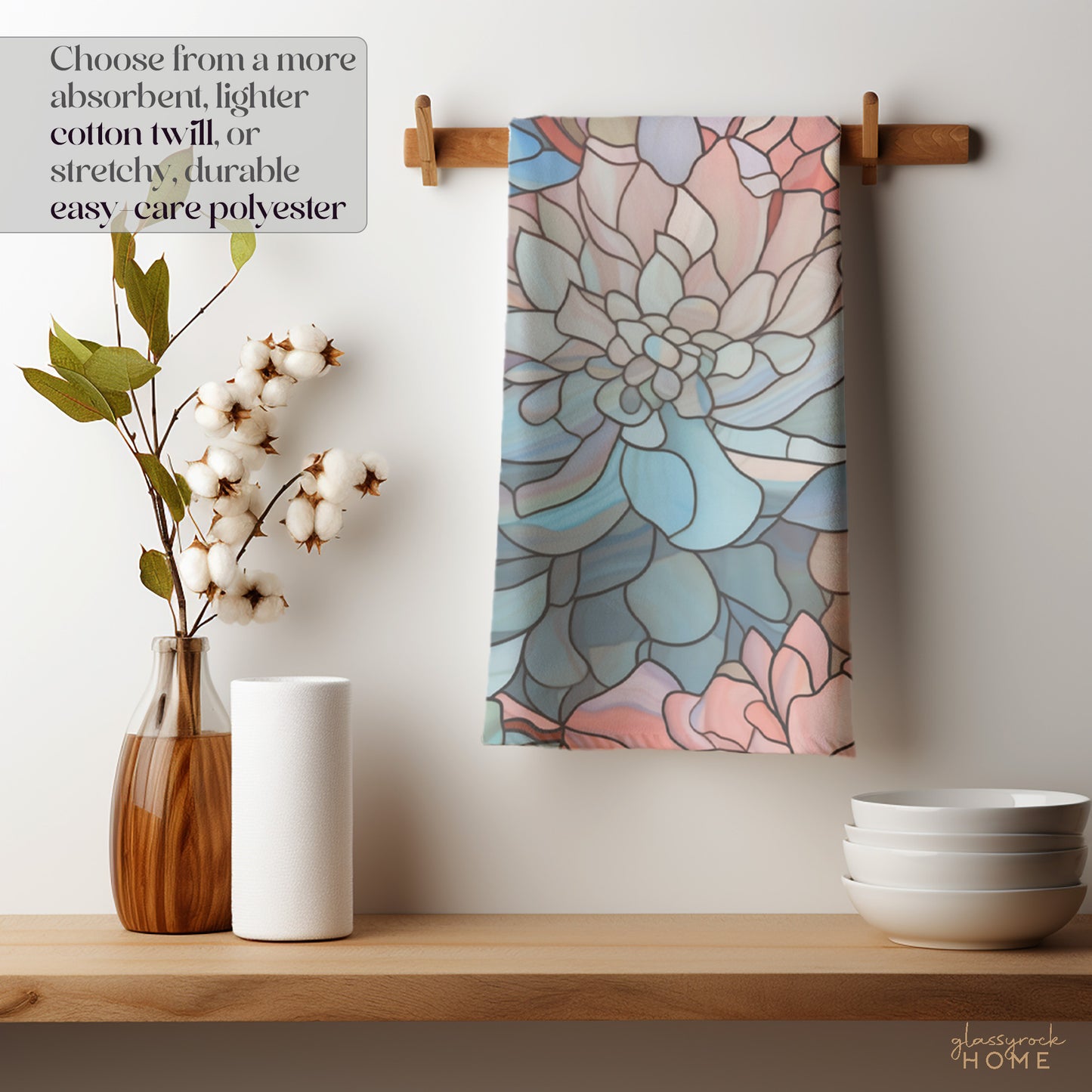 The Stained Glass Dark Flowers Dish Towel, with a floral pattern and pastel colors, hangs on a wooden peg, making for a charming housewarming gift. Below it are cotton branches in a vase, a white rolled-up towel, and stacked bowls. Choose from absorbent cotton twill or durable polyester options.