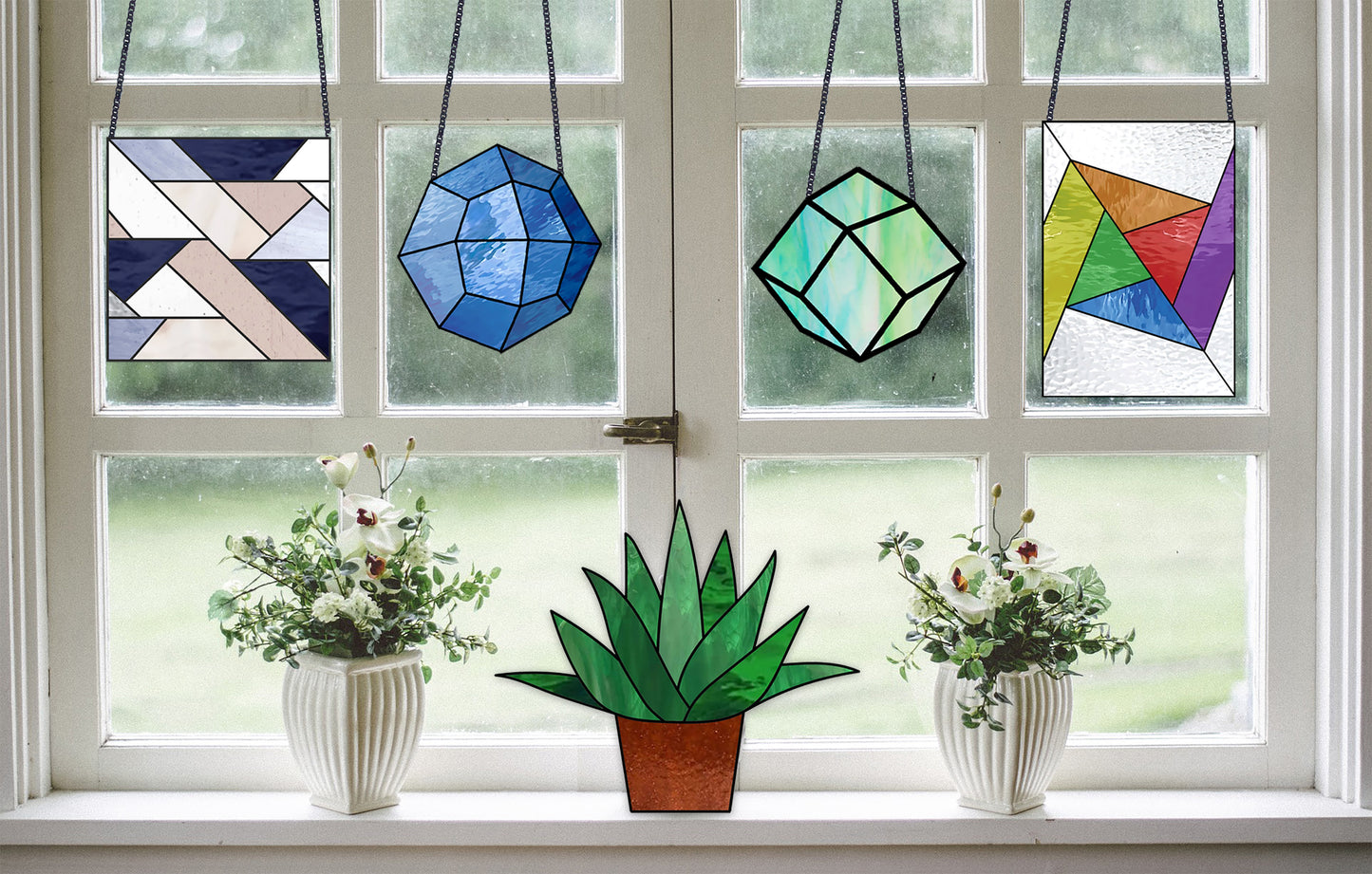 Geometric stained glass patterns from the beginner mega pack shown in a white windowsill with plants