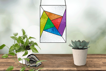 Beginner stained glass pattern of an abstract rainbow pinwheel, instant PDF download, shown hanging in a window with plants